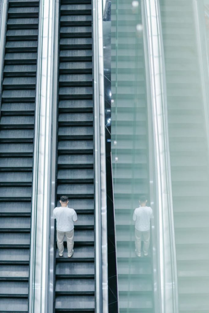 The image features a modern escalator in a public space, highlighting clean lines, symmetry, and a lone figure riding it.